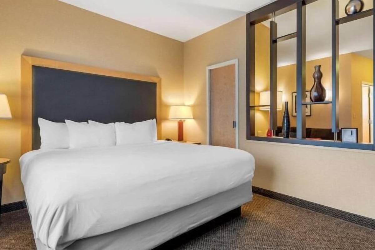 A hotel room with a large bed, two bedside tables with lamps, a mirror, and a view of the room's interior.
