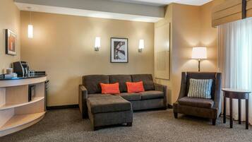 Habitación de hotel con sofá, reposapiés, sillón y una mesita. Se observa un reloj en la pared y dos apliques.