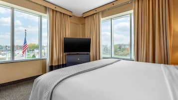 Habitación de hotel con una cama grande, un televisor de pantalla plana y vistas de la ciudad a través de amplias ventanas.