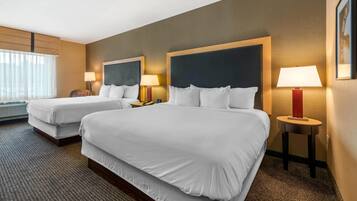 Habitación de hotel con dos camas, un ventanal con cortinas translúcidas, suelo alfombrado y lámparas de noche.