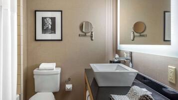 A modern bathroom with a toilet, sink, and two mirrors. There is a framed picture on the wall and a towel on the counter.