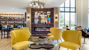 A modern lounge area with yellow armchairs, a fireplace, and a wall with various colorful tiles. - Cambria Hotel Akron - Canton Airport (Uniontown)