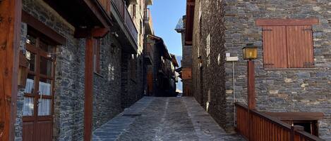 A narrow cobblestone street flanked by stone buildings with wooden balconies and shutters.