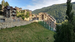 A hillside village with stone buildings, a stone wall, and a green area. - Wuau! Apartaments Font del Poble (Ransol)