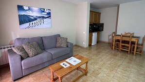 A living room with a grey sofa, a wooden coffee table, and a painting of a snowy mountain scene. - Wuau! Apartaments Font del Poble (Ransol)