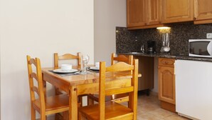 A small kitchen with wooden cabinets, a dining table with chairs, a coffee maker, and a microwave. - Wuau! Apartaments Font del Poble (Ransol)
