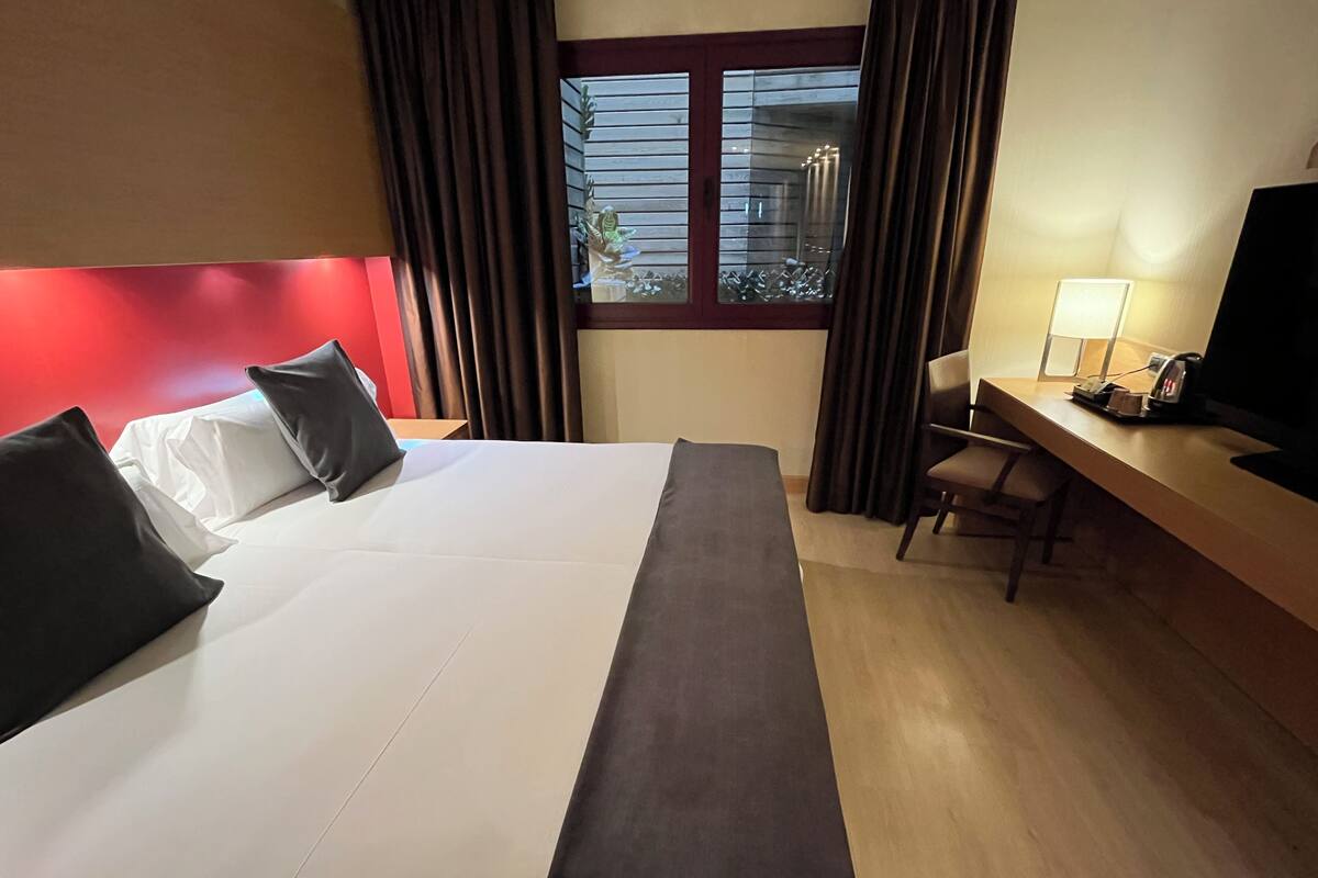 Une chambre d’hôtel avec un grand lit, un bureau, une chaise, une télévision et une fenêtre avec des rideaux.