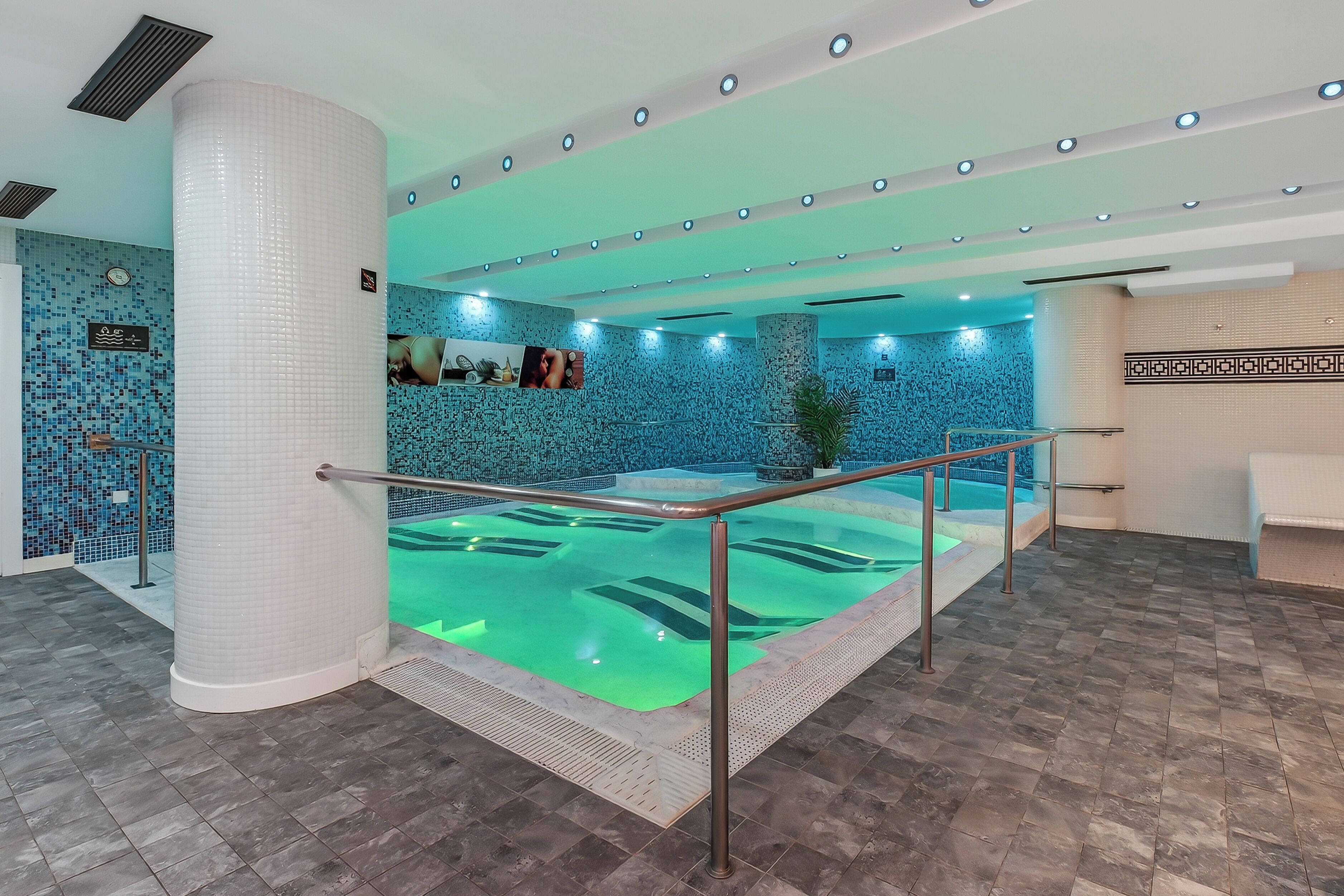 A swimming pool with a glass barrier, tiled walls, and a ceiling with recessed lighting.