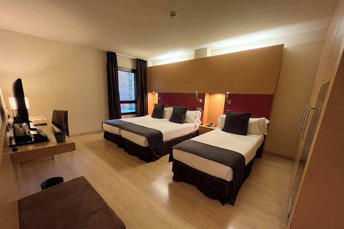 Une chambre d’hôtel avec deux lits, un bureau avec un ordinateur, une chaise et une petite table.