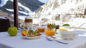 A breakfast table with fruit, juice, and a bowl of cereal, set against a snowy mountain backdrop. - Wuau! Hotel Galanthus & Spa (Soldeu)