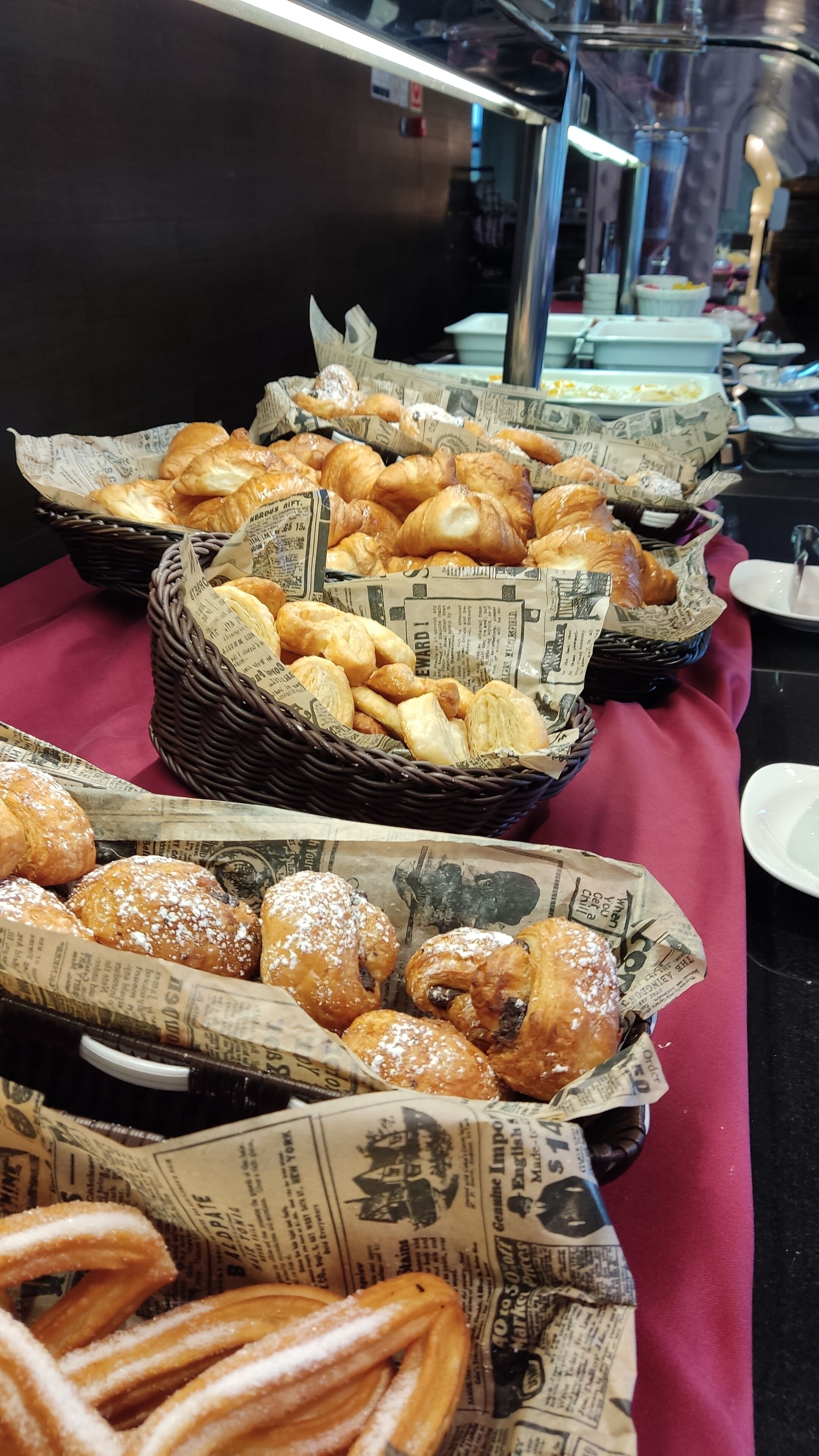 A buffet table with various pastries in baskets lined with newspaper.