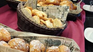 A buffet table with various pastries in baskets lined with newspaper.