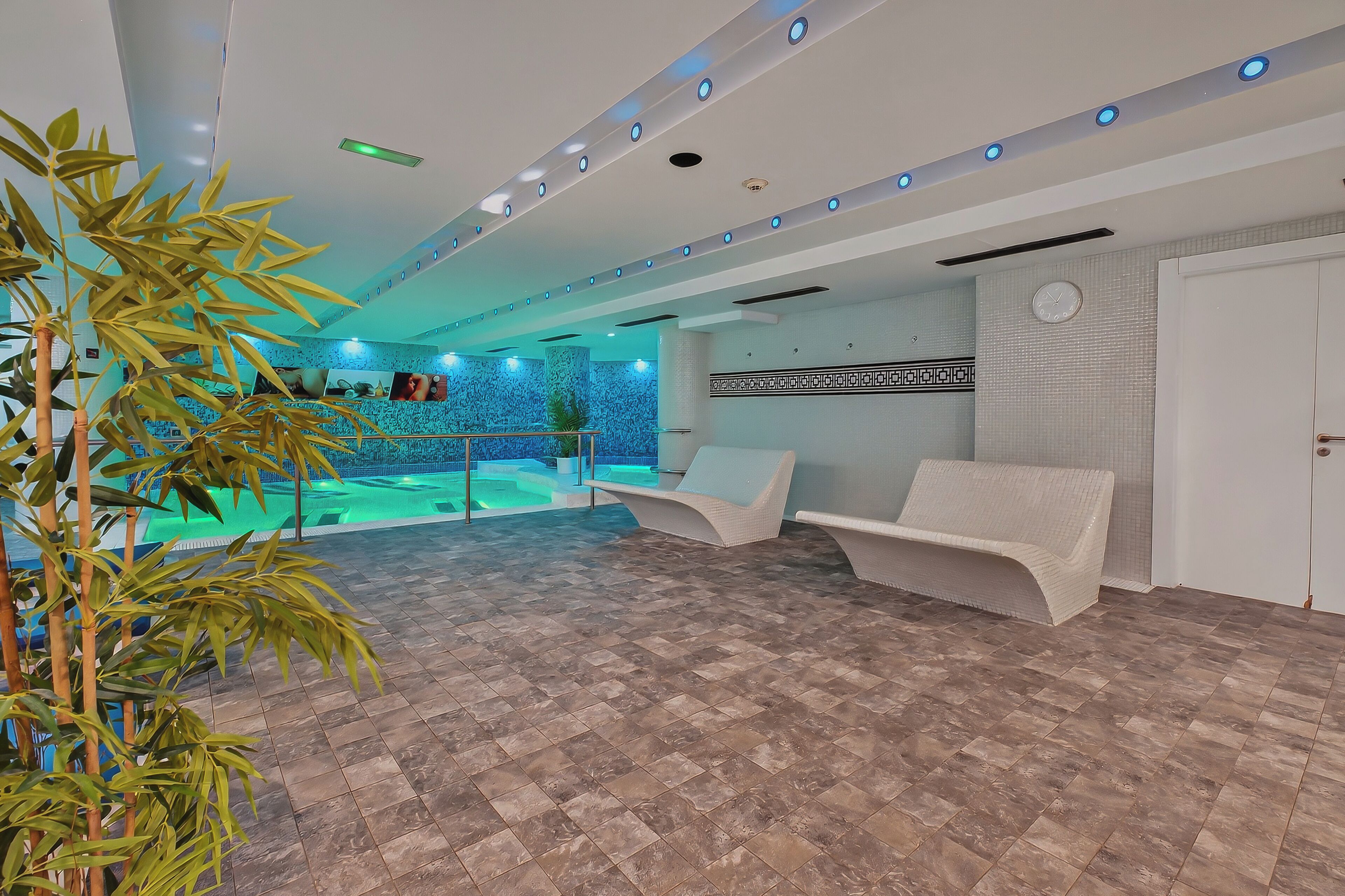 A modern indoor pool area with seating and a clock on the wall.
