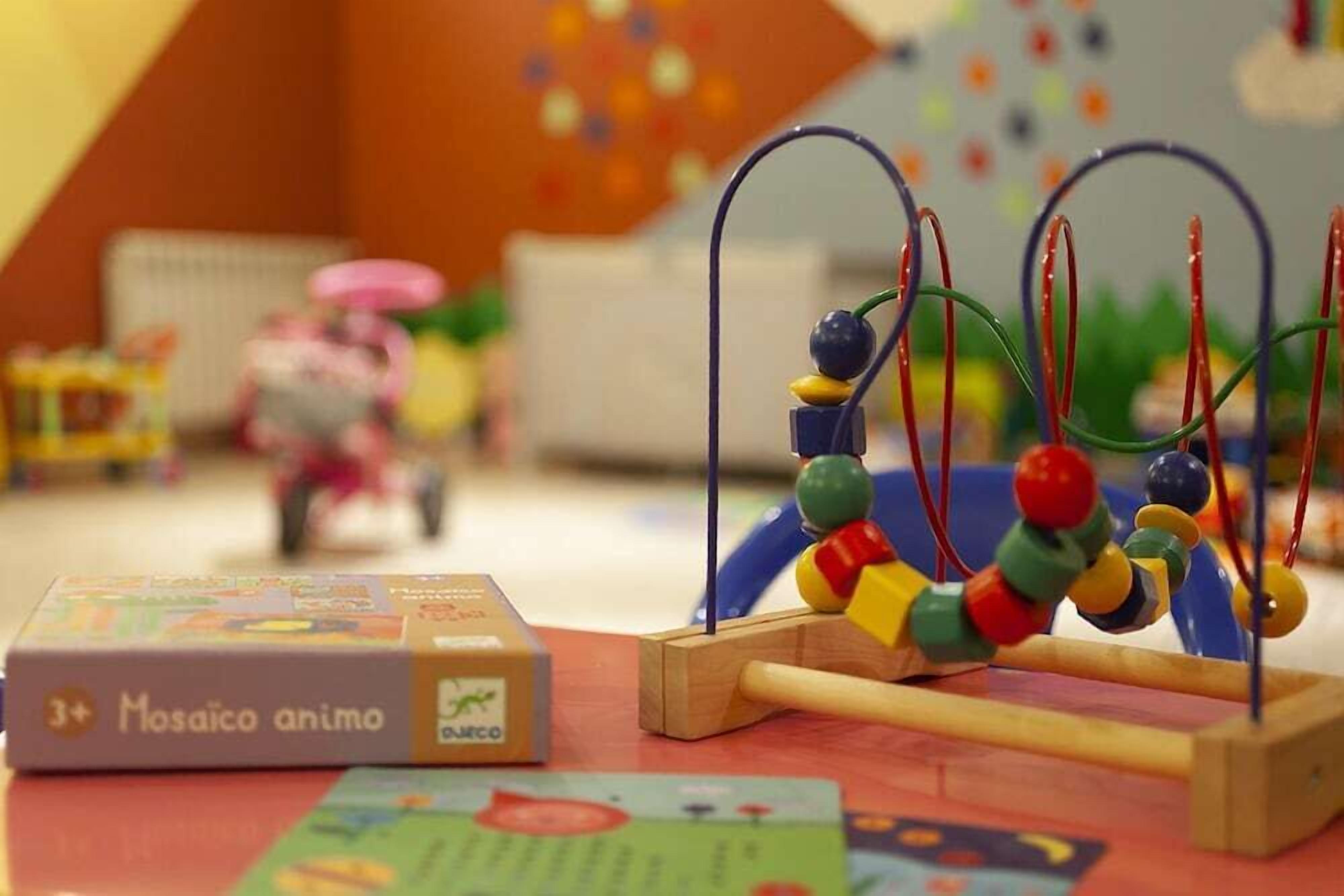 A children's toy with colorful beads and a wooden base, a book titled "Mosaico animo," and a toy car in the background.