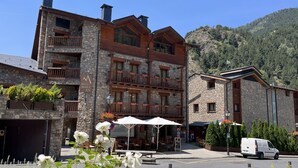 Un hotel de varios pisos con fachada de piedra y madera, balcones con macetas y una vista despejada de las montañas circundantes.