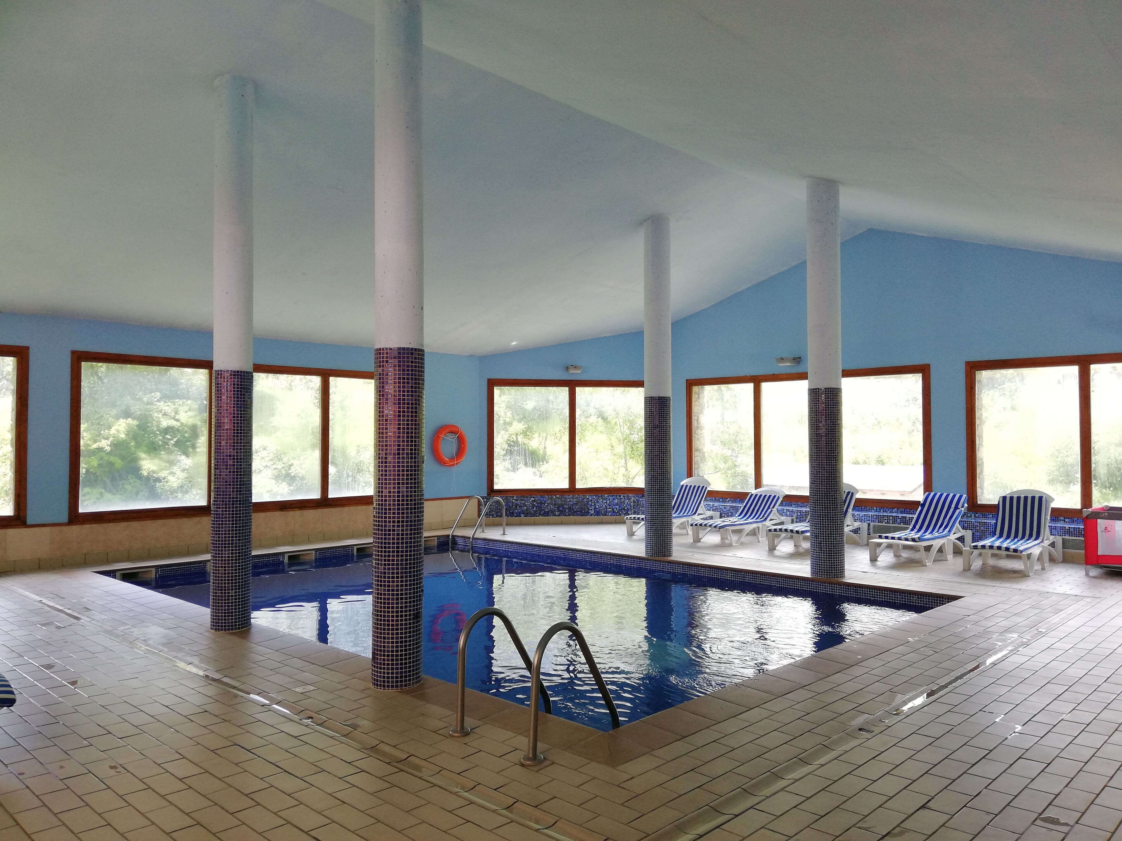 Una piscina interior con paredes de azulejos y ventanas, rodeada de sillas de descanso.