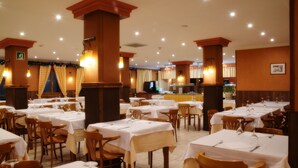 Un restaurante con varias mesas y sillas, cada conjunto con manteles blancos y cubiertos.