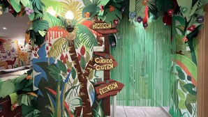Una habitación con un mural temático de selva, una cama y una cortina verde.