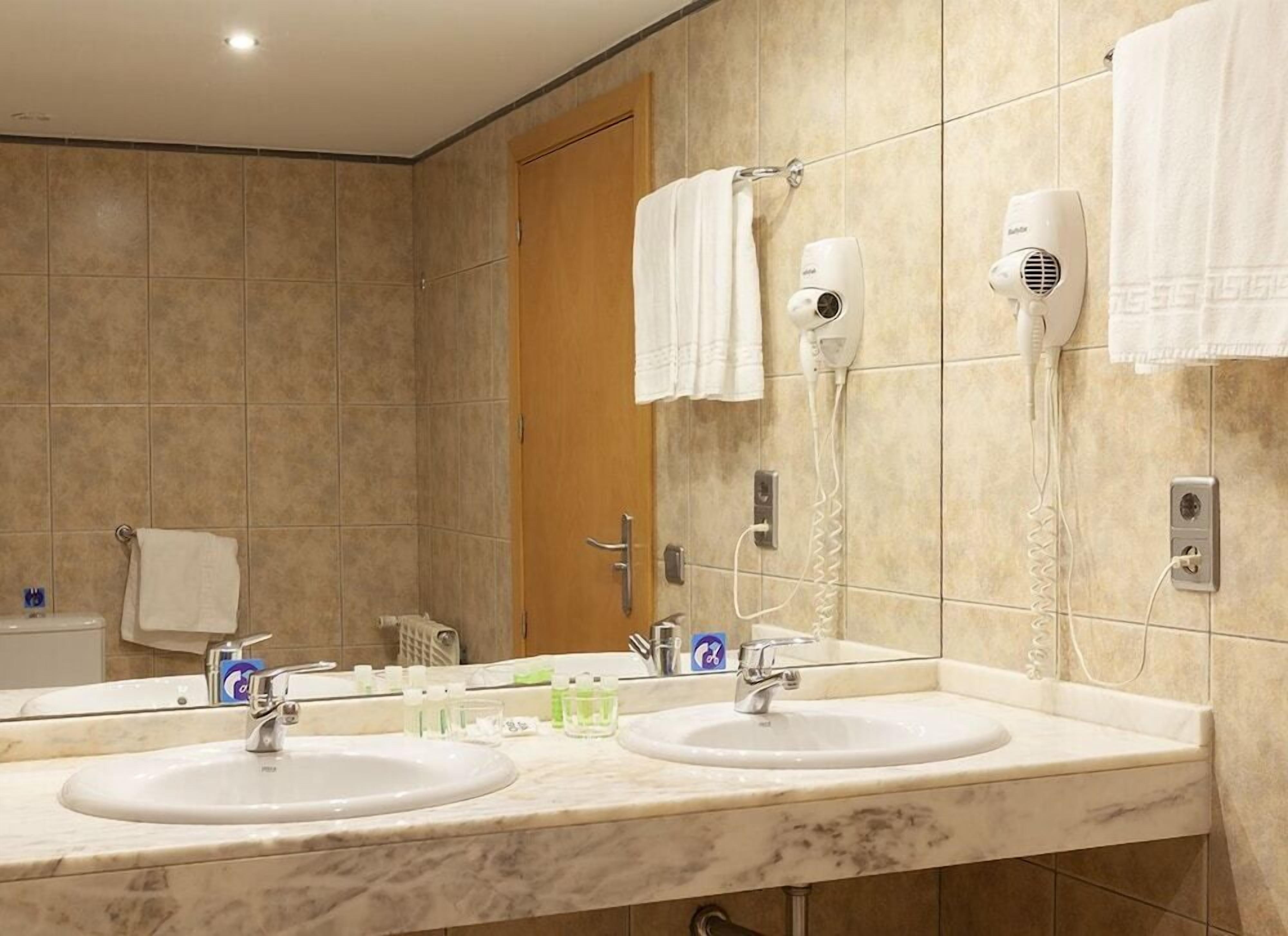 Un baño de hotel con dos lavamanos, un espejo, un perchero para toallas y un secador de pelo.
