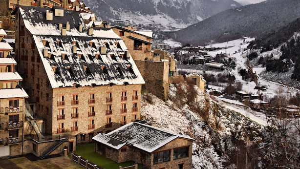 Un edificio de piedra tradicional con varios balcones y un techo empinado, rodeado de un paisaje montañoso nevado.