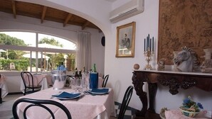 Un comedor con una mesa dispuesta para cuatro, rodeada de sillas, un aparador decorativo y una ventana con cortinas.