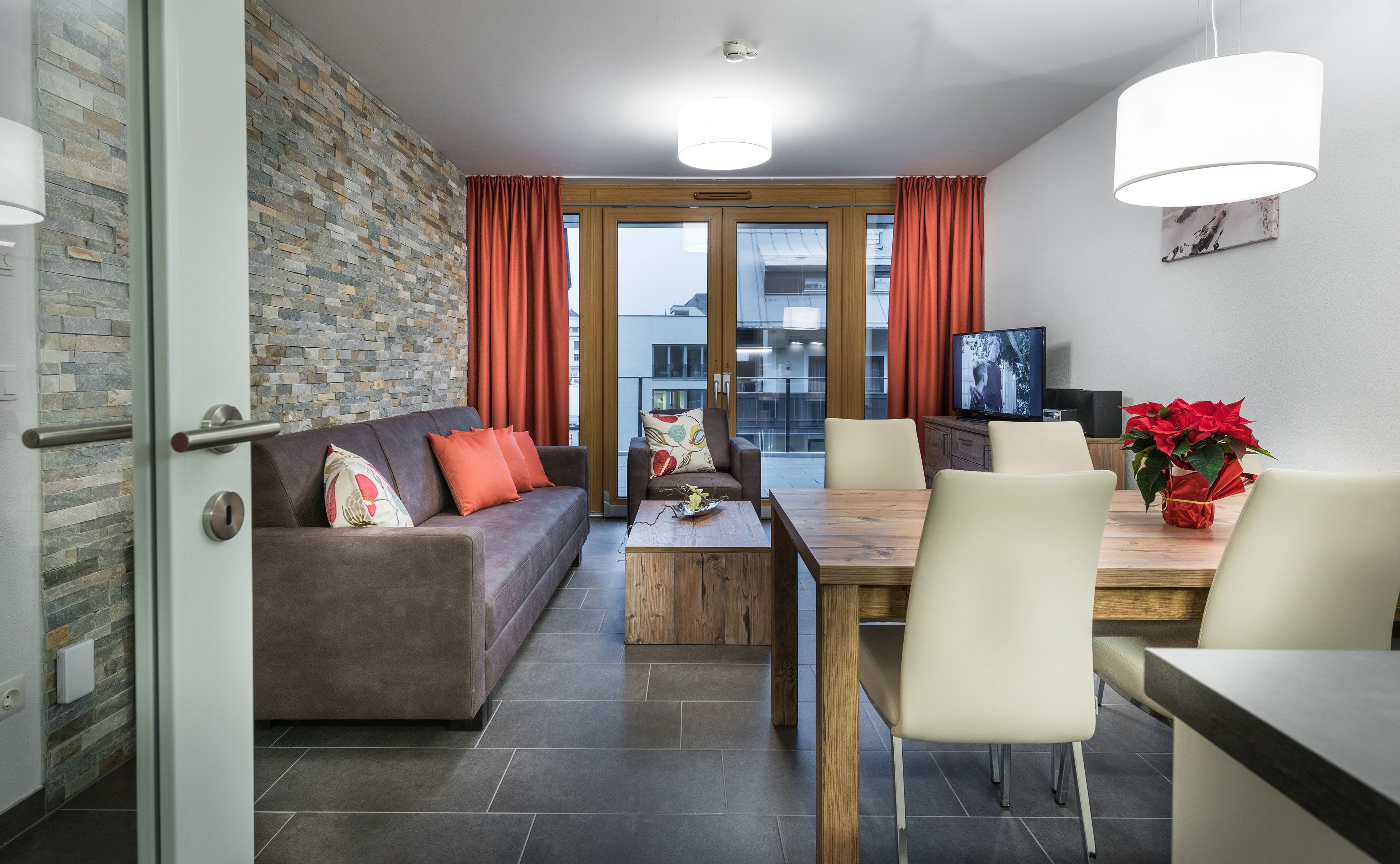 Una sala de estar moderna con sofá, mesa de centro, mesa de comedor y sillas. Hay un televisor sobre un mueble de madera, y una planta en maceta sobre la mesa.