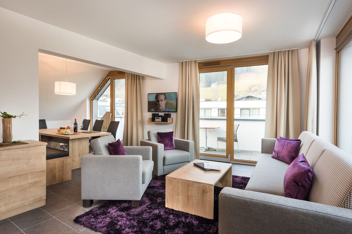 A modern living room with a sofa, armchairs, a coffee table, and a TV mounted on the wall.
