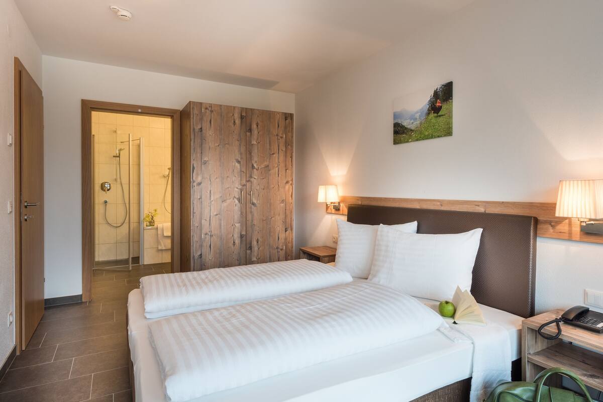 A hotel room with a large bed, wooden panel wall, and a painting of a landscape.
