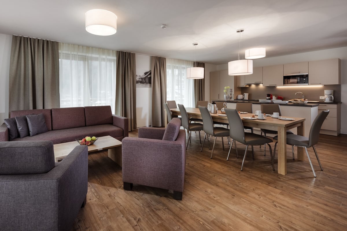 A modern living room with a sofa, armchairs, a coffee table, and a dining area with chairs and a table.