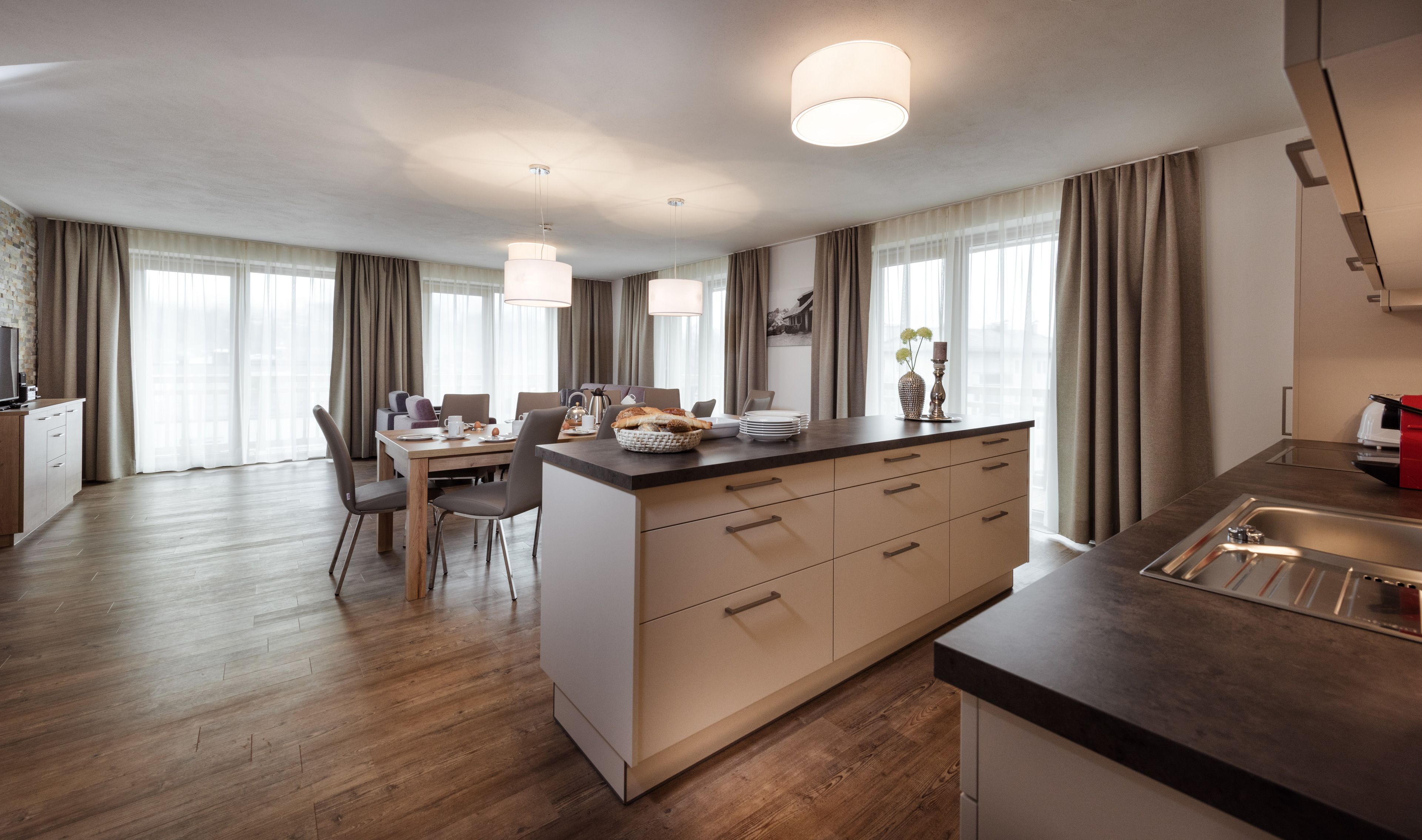 A modern kitchen with a central island, wooden flooring, and a dining area with a table and chairs.