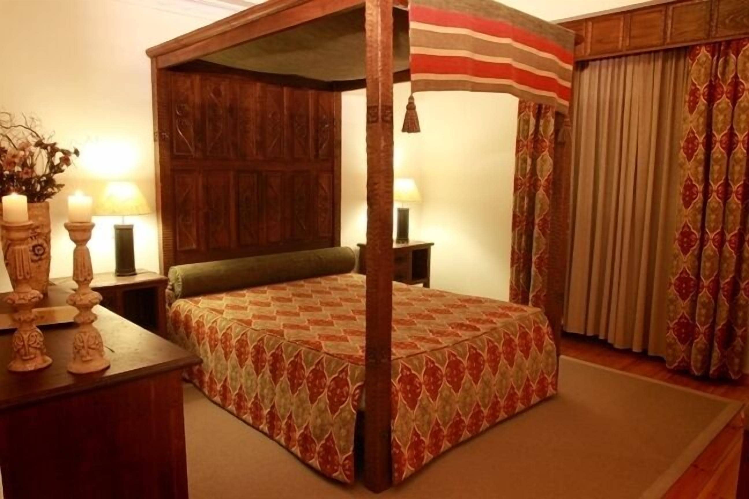 Una cama con dosel, con colcha estampada, cabecera de madera y dos lámparas de noche.