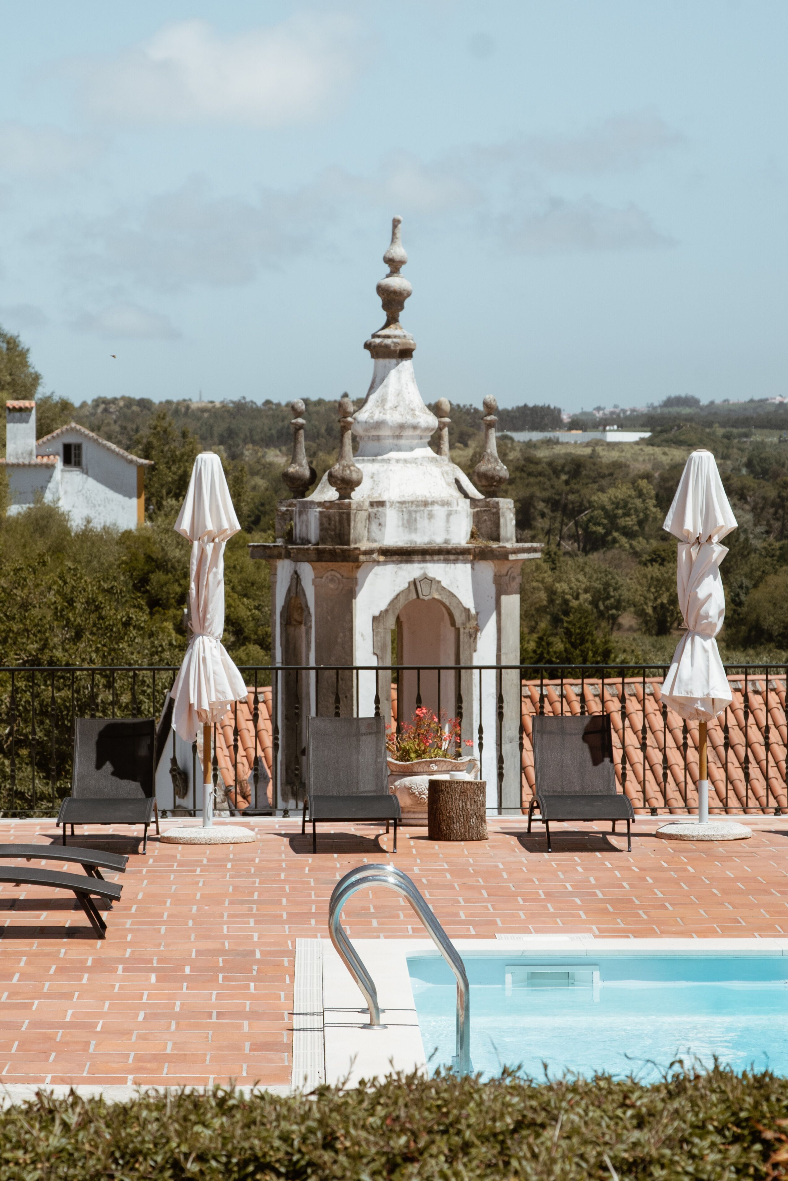 A rooftop pool area with lounge chairs and umbrellas, surrounded by a tiled deck and a decorative gazebo.