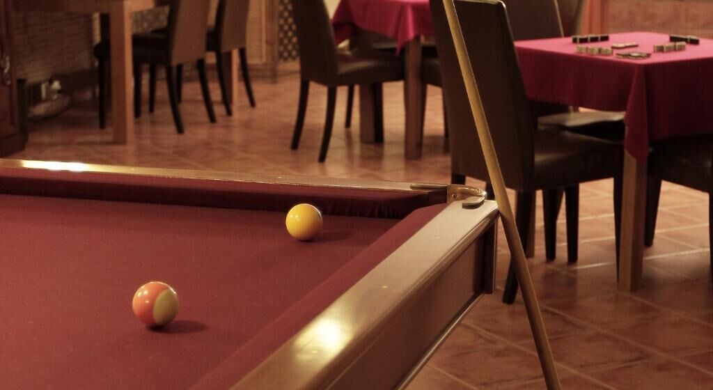 A pool table with balls, a dining area with tables and chairs, and a brick wall in the background.
