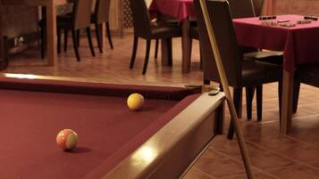 A pool table with balls, a dining area with tables and chairs, and a brick wall in the background.