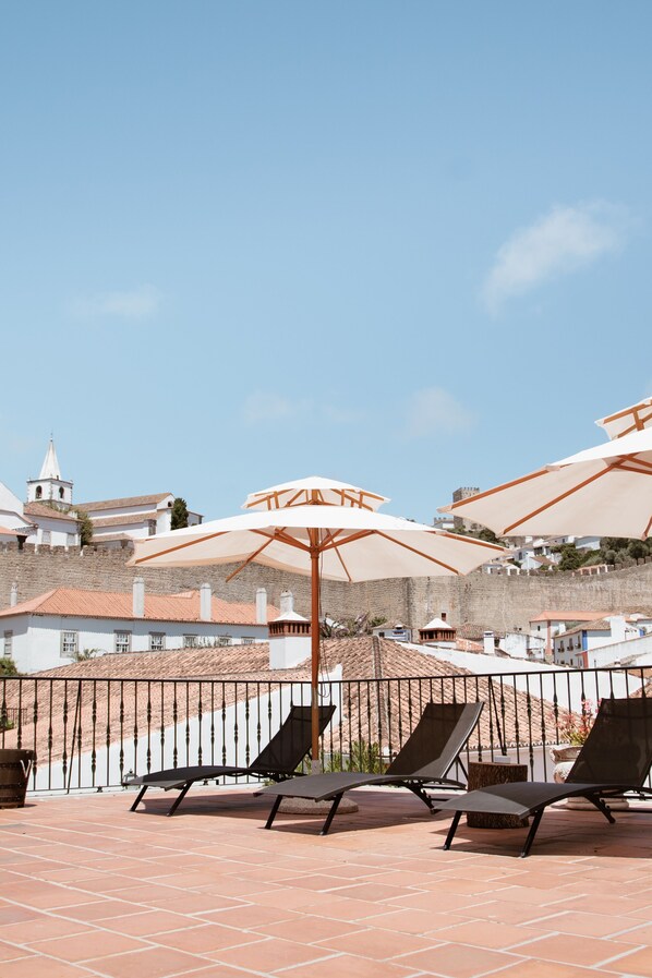 Una terraza con sillones y sombrillas, con vistas a un pueblo histórico con edificios y una iglesia.