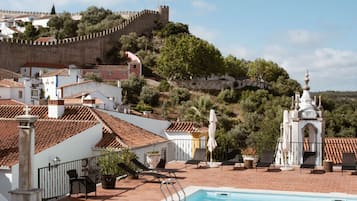 A swimming pool with a view of a historic hilltop fortress and terracotta-roofed buildings.