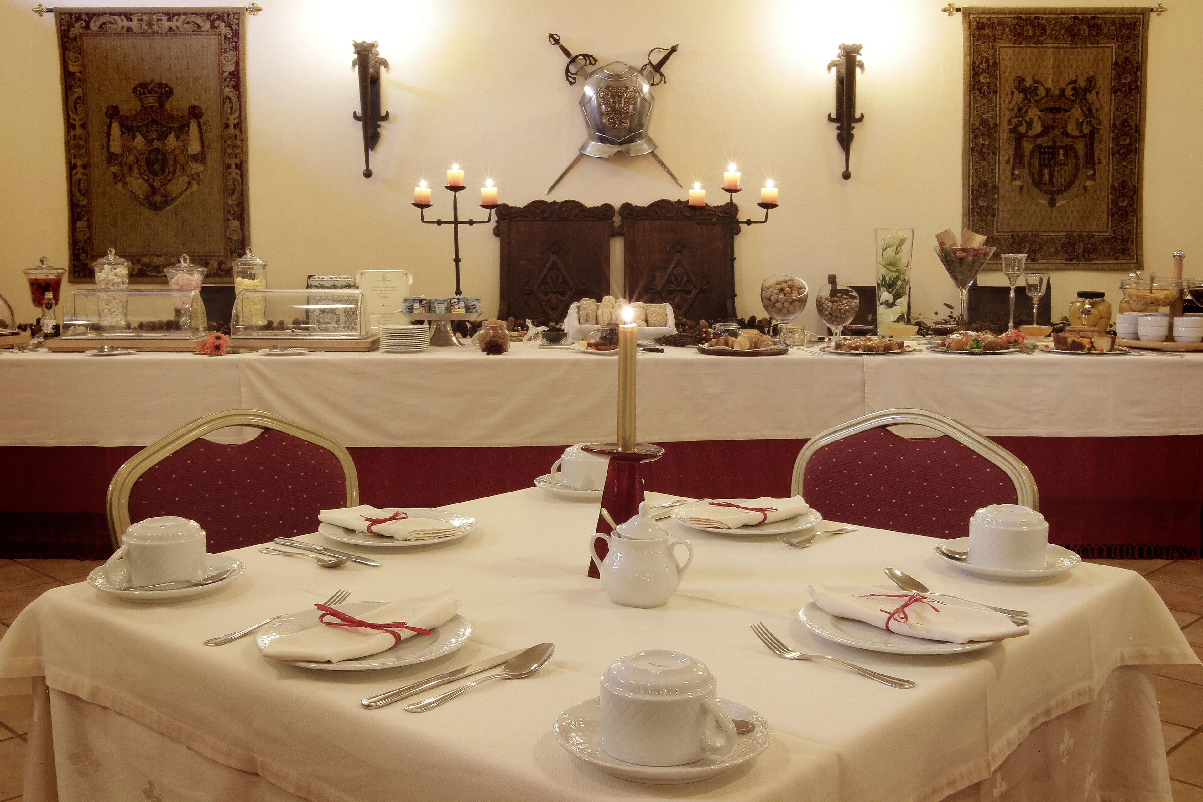 Una mesa de banquete dispuesta con vajilla blanca, velas y tapices colgados en la pared.