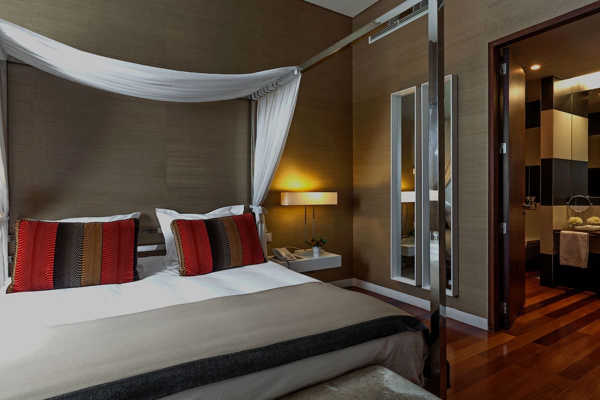 A modern hotel room with a four-poster bed, a bedside table with a lamp, and a large mirror.