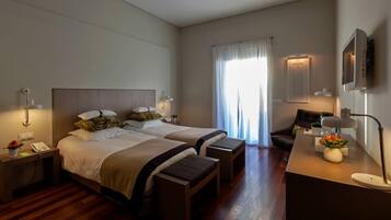 A hotel room with two beds, a desk with a lamp, a chair, a nightstand, and a window with curtains.