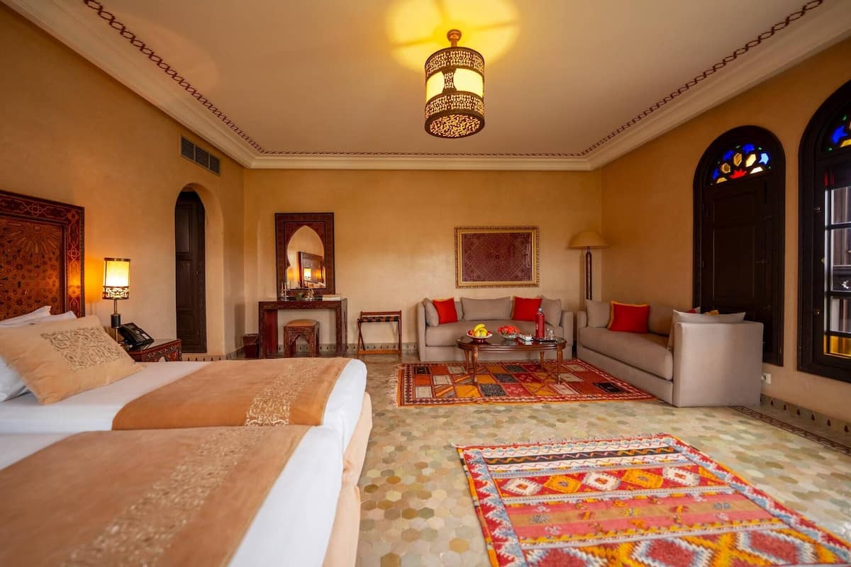Quarto de hotel com duas camas, um sofá, uma mesa de centro e um tapete decorativo.