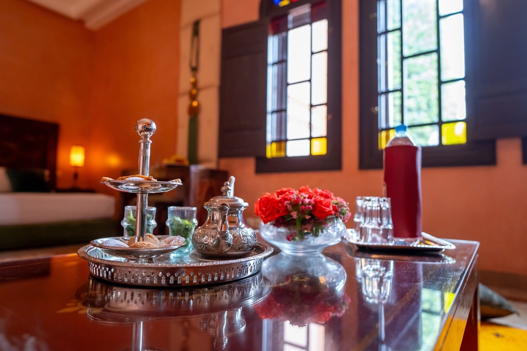 A table with a silver tray, a teapot, a glass of water, a red candle, and a vase with red flowers.