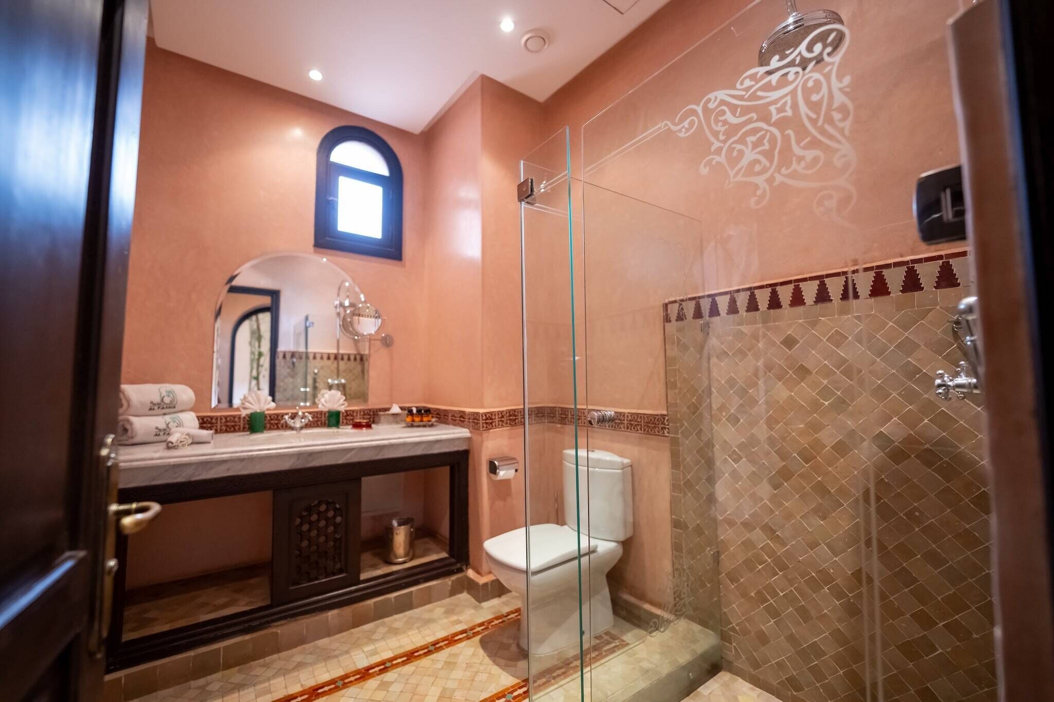 A bathroom with a glass-enclosed shower, a toilet, and a vanity with a mirror and towel rack.