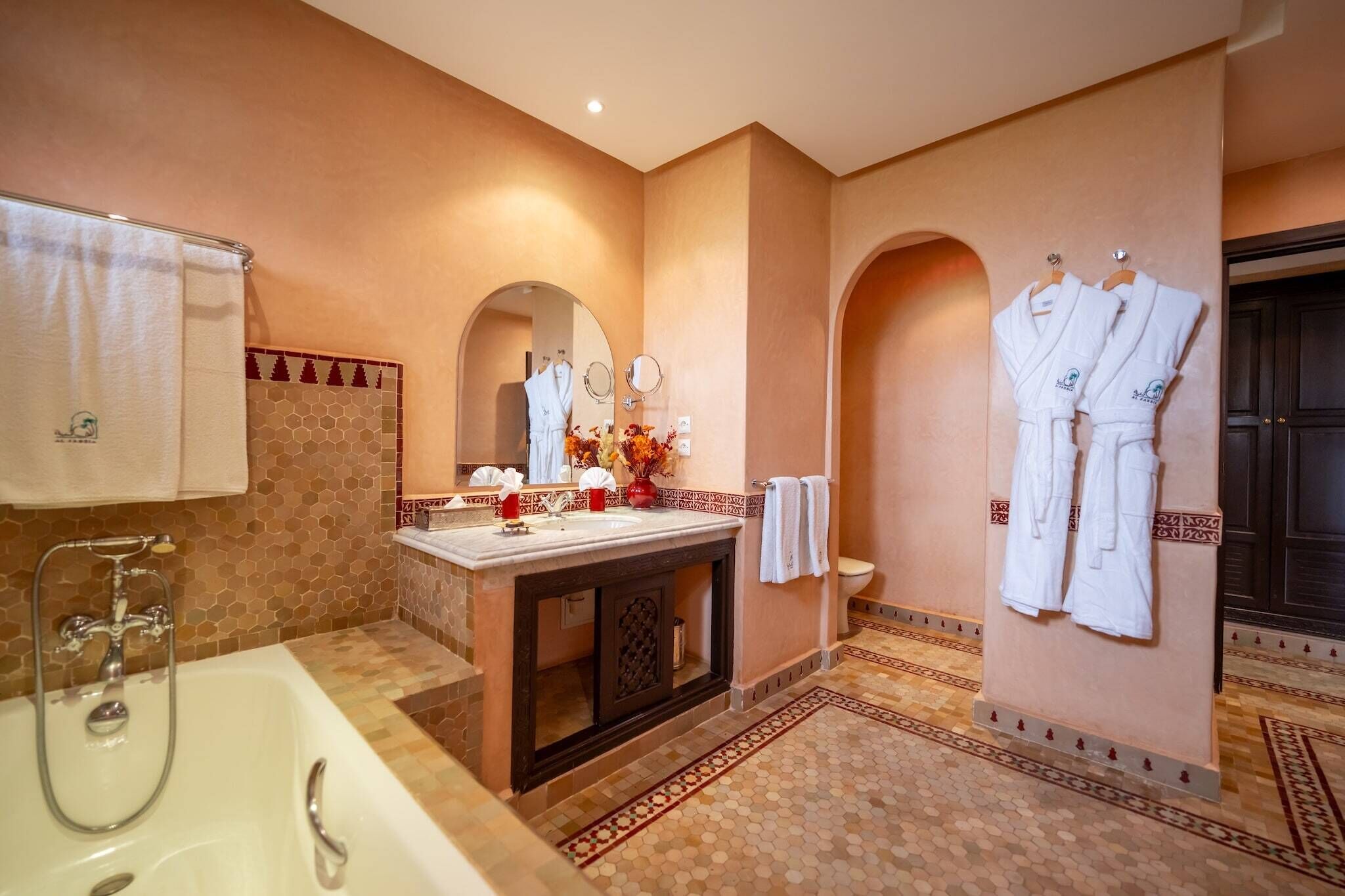 A bathroom with a bathtub, sink, and two mirrors. There are towels and robes hanging on the wall.