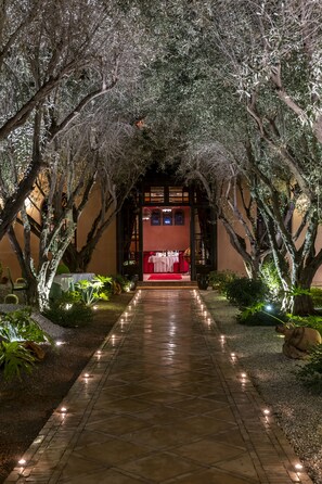 Stroll along the beautifully paved pathway, lined with blooming trees and soft lighting, to a traditional building with a cozy dining area.