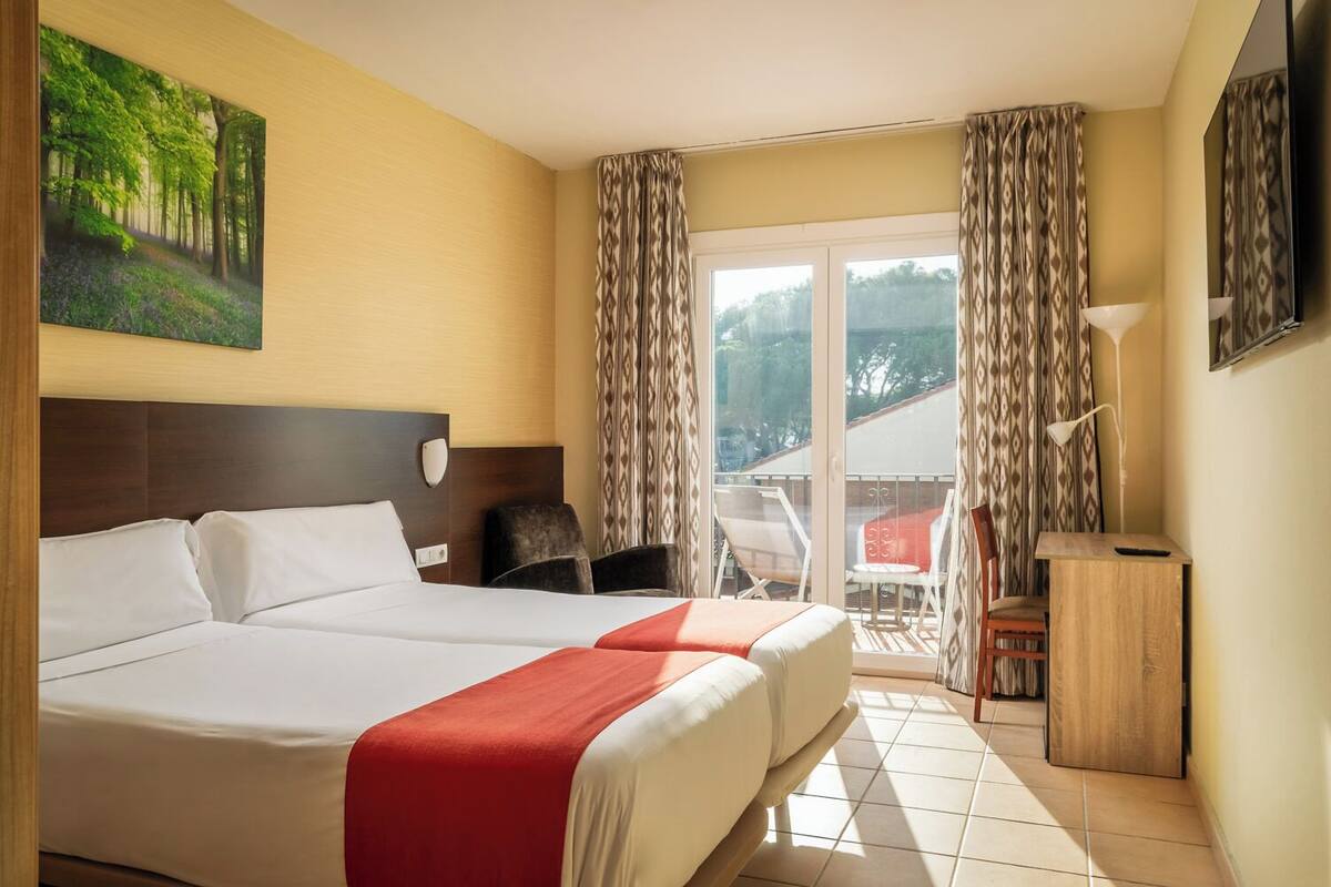Une chambre d’hôtel avec un grand lit, un bureau, une chaise, un balcon avec vue et un tableau au mur.