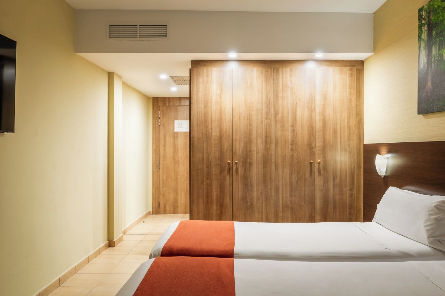 Una habitación de hotel con una cama, un armario y un cuadro en la pared.