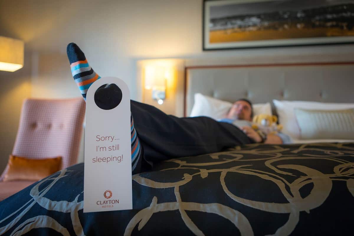 A hotel room with a bed, a pillow, a blanket, a chair, and a sign with text.
