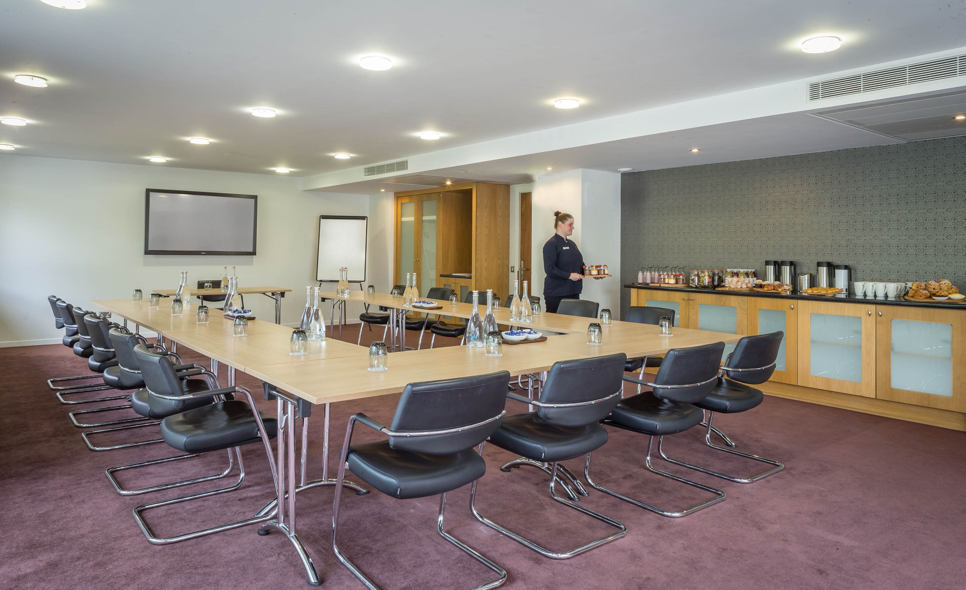 A conference room with a long table, chairs, a whiteboard, and a kitchenette area.