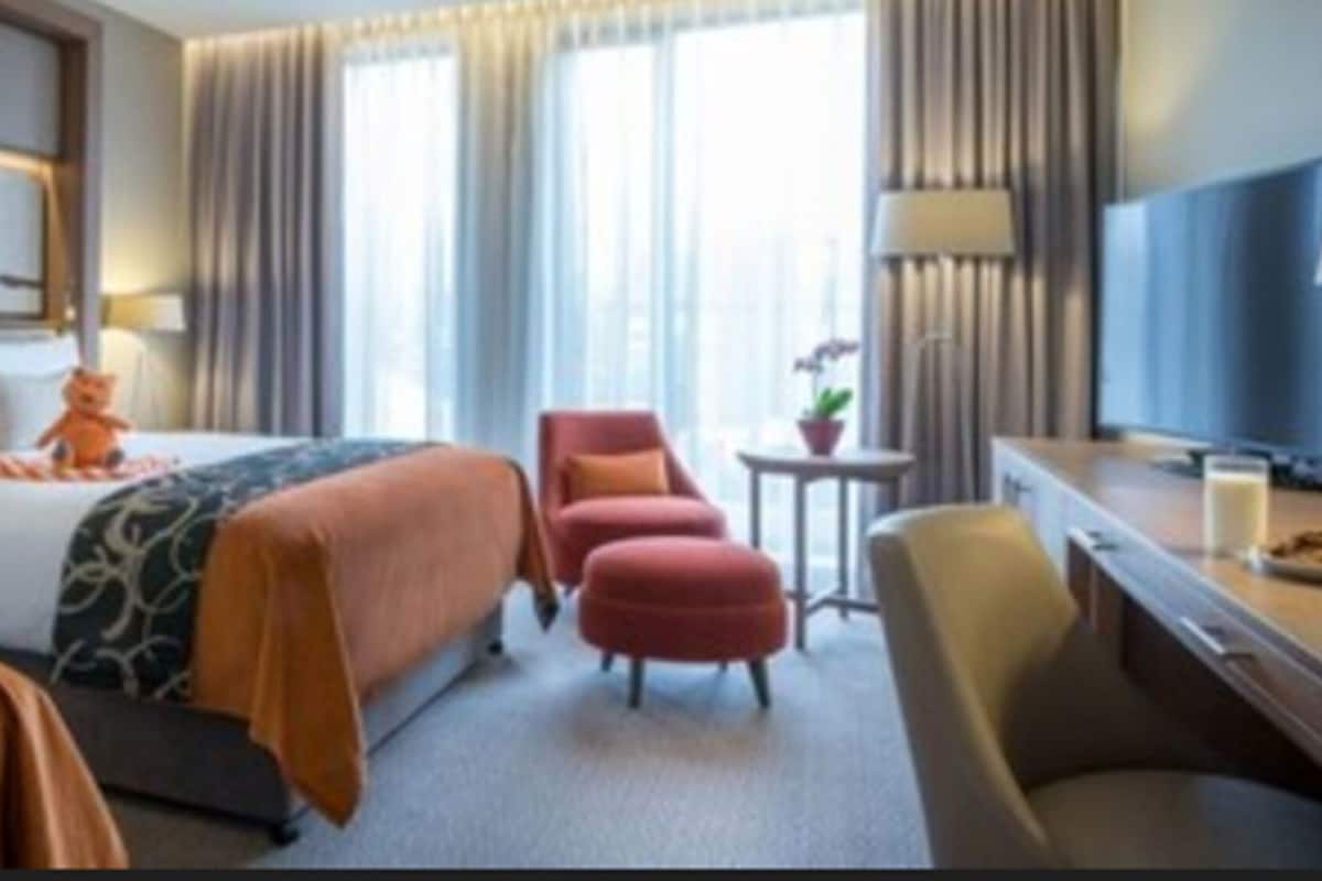 A hotel room with a bed, two armchairs, a desk with a TV, and a small table with a lamp.
