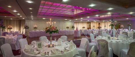 Un salón de banquetes con mesas redondas, manteles blancos y sillas cubiertas con tela blanca.